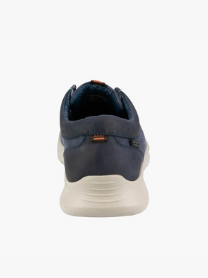 A rear view of the Florsheim Bushwacker Canvas Slip On in navy blue shows a casual sneaker with a white sole, subtle stitching, and small orange accents on the heel tab and upper back, crafted from organic cotton for comfort.