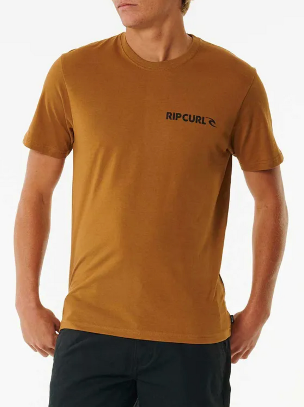A person stands against a plain white background wearing a mustard yellow Rip Curl Brand Icon Tee (100% cotton) and black pants, with their hands by their sides.