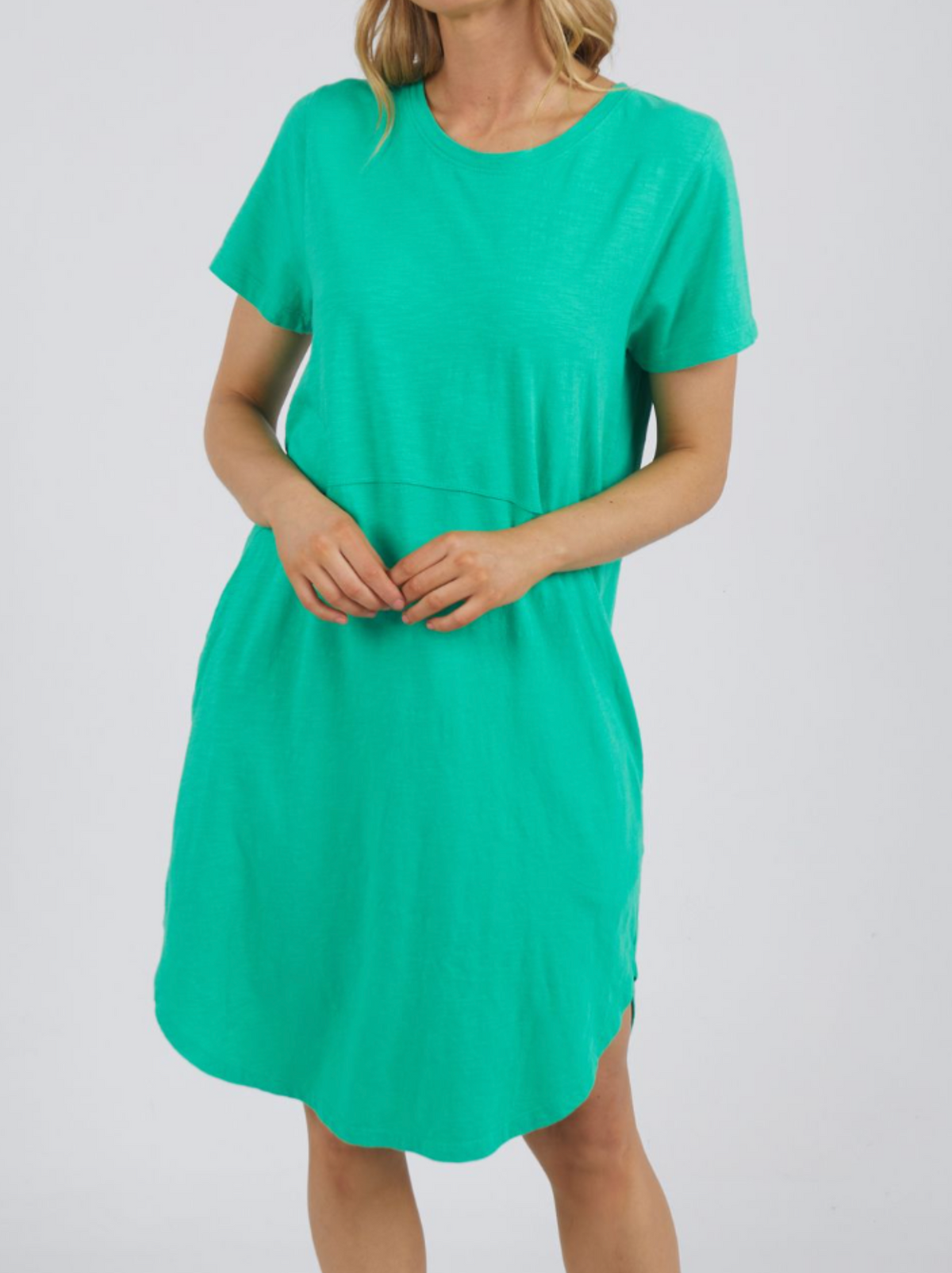 Against a plain light background, someone wears the vibrant Foxwood Bay Dress. Made from 100% cotton, it features a relaxed fit, round neckline, and slightly curved hem, with the individual's hands gently clasped in front.