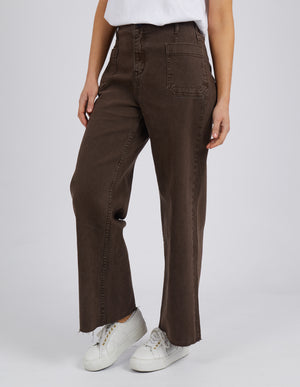 A person wears Foxwood Eddie Wide Leg Jeans, featuring a high waist, wide legs, and raw edge detailing. Paired with a white t-shirt and white sneakers, the jeans with front pockets create a stylish ensemble against a plain gray background.