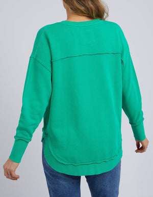 Someone wearing a bright green Foxwood Simplified Crew and blue jeans, shown from the back, with loose sleeves, visible seam details, subtle Foxwood embroidery, and crafted from soft 100% cotton.