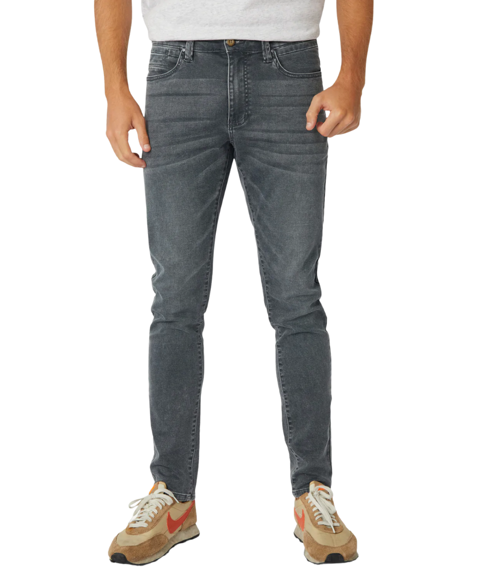 A person stands against a white background, wearing a light gray t-shirt with Industrie branding, complemented by Industrie The Denim Drifter NC Pant in faded gray skinny fit and beige sneakers featuring orange swooshes.