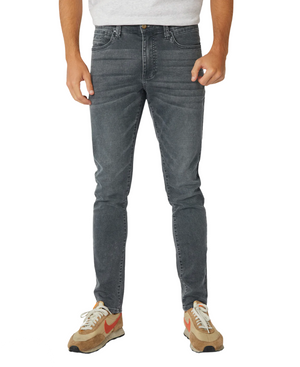 A person stands against a white background, wearing a light gray t-shirt with Industrie branding, complemented by Industrie The Denim Drifter NC Pant in faded gray skinny fit and beige sneakers featuring orange swooshes.