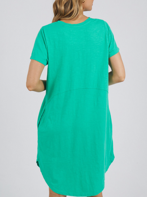 A person is shown from the back wearing a short-sleeved Foxwood Bay Dress in a plain, light background. The dress is 100% cotton jersey, loose-fitting with a slightly curved hem and visible waist seam.