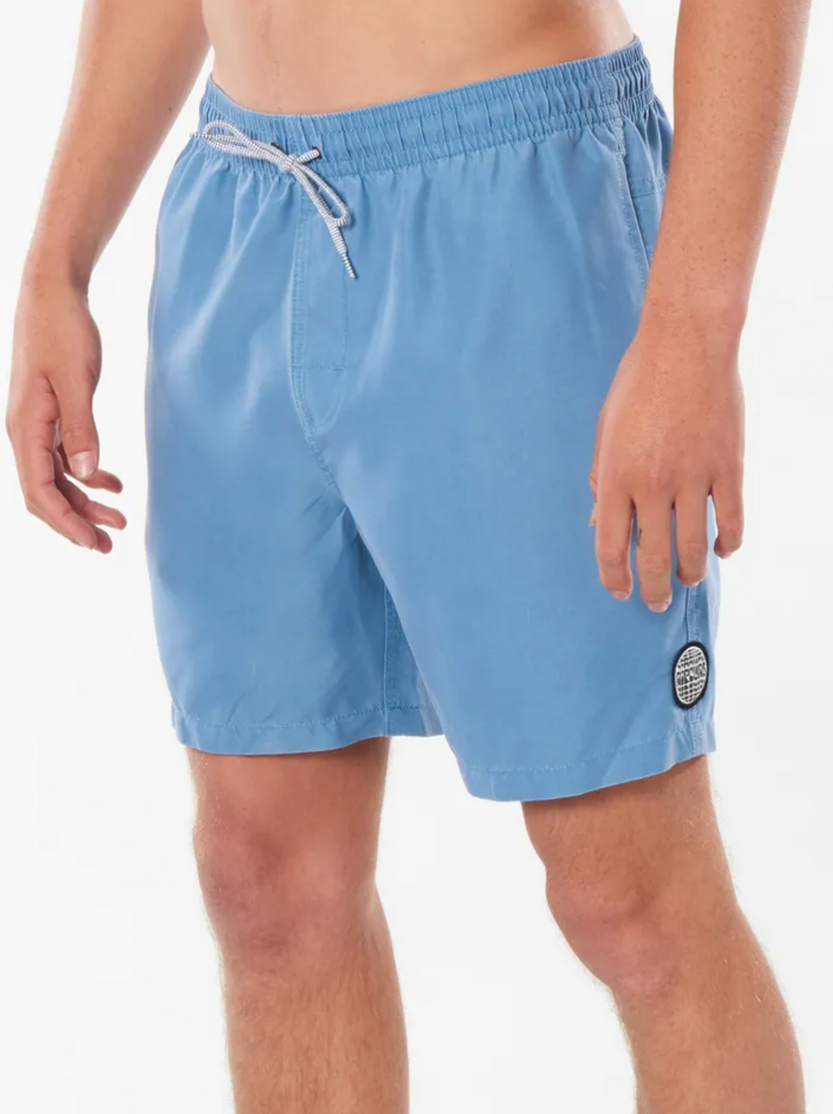 Someone wears Rip Curl Bondi Volley shorts in light blue, featuring an elastic waistband, drawstring, and a small round patch on the left leg. Ideal for the beach, they're set against a plain white background.