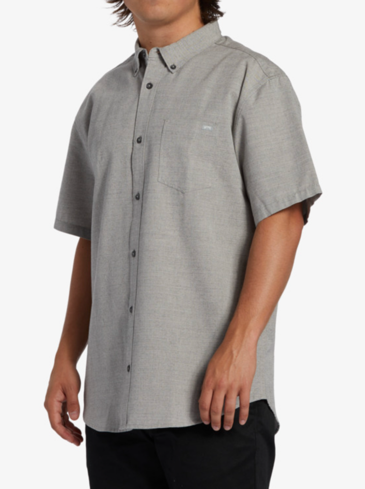 A person wears the Billabong All Day Short Sleeve Shirt in light gray, made from soft cotton-polyester fabric with a chest pocket and black buttons, standing against a plain white background.