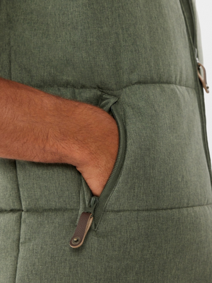 A close-up of a hand in the zippered pocket of a green RM Williams Patterson Creek Vest, highlighting its quilted puffer design and water- and winter-resistant fabric texture.