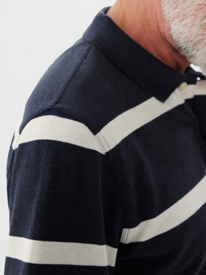 Close-up of an older man wearing an RM Williams Rod Polo in navy blue with wide white stripes. The focus is on the shoulder and collar, showcasing the soft cotton pique fabric, while his head is slightly turned to reveal a gray beard.