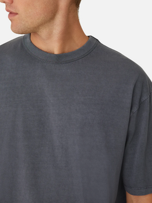 A person wearing the Industrie The Del Sur Tee is angled to the side, highlighting its oversized fit. The loose, faded blue-gray T-shirt, made of 100% cotton, stands out for its texture and comfort against a plain white background.