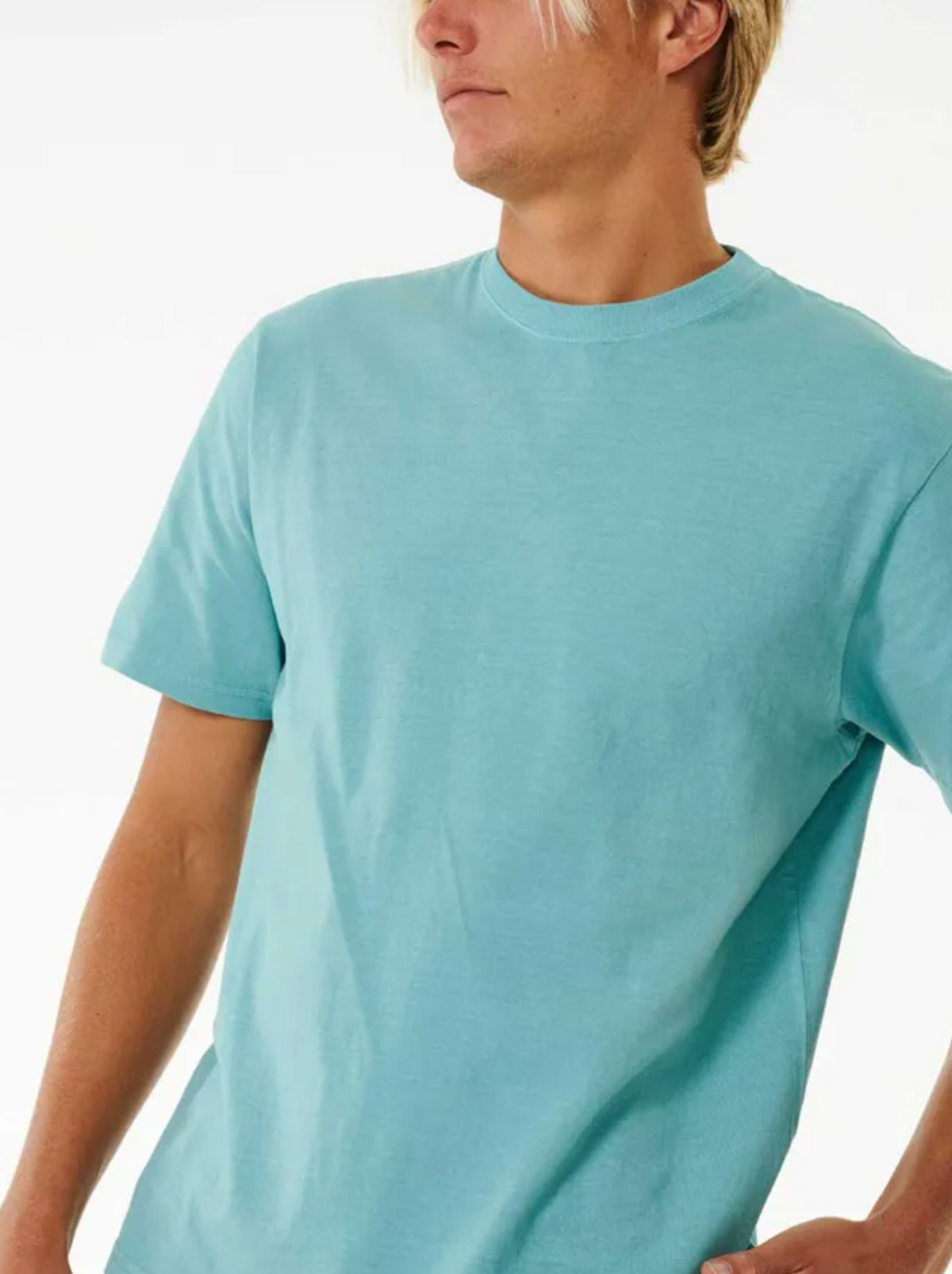 A light-haired person wears a light blue, short-sleeved Rip Curl Plain Wash Tee, showcasing a casual vibe. The relaxed fit complements their slightly turned stance against a plain white background.