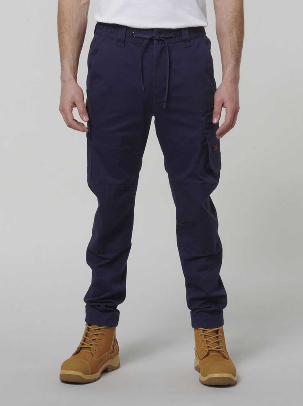 Someone is wearing Hard Yakka Tough Maxx navy cargo pants with many pockets, a white T-shirt, and tan work boots. This durable ensemble contrasts with the plain gray background and provides both style and sun protection for a long day outdoors.