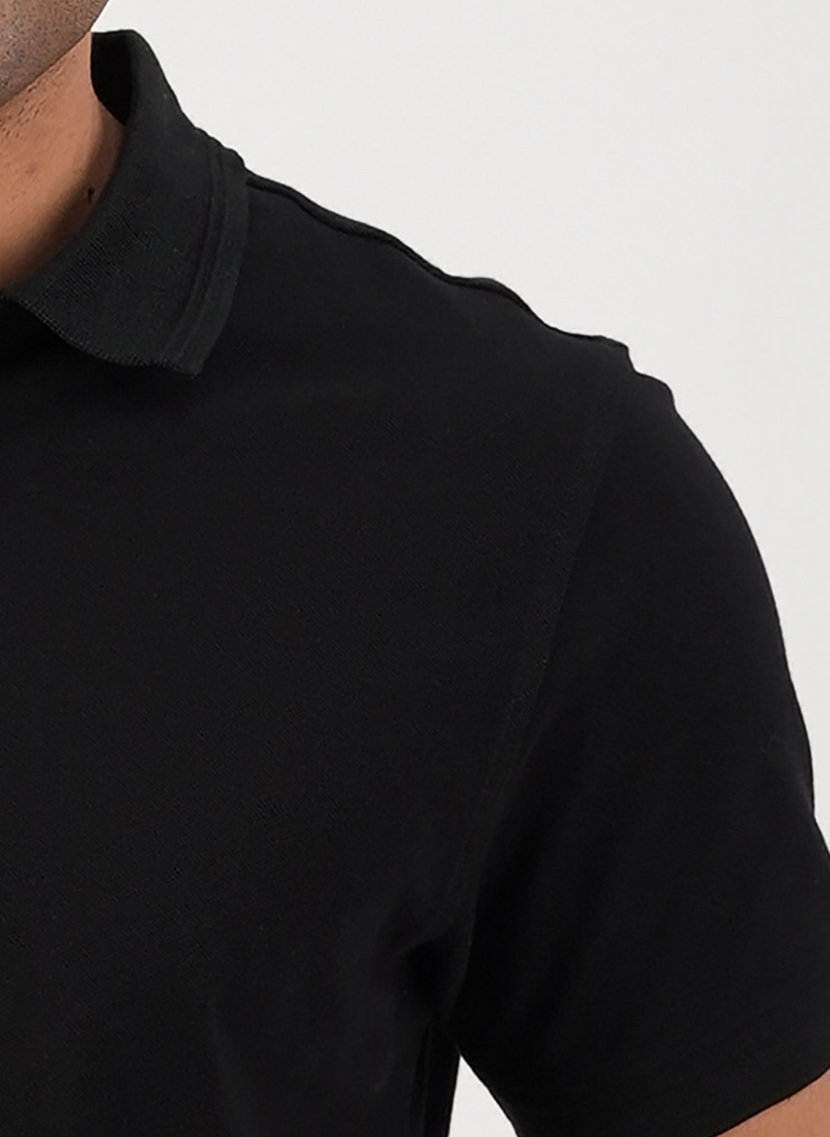 Close-up of a person wearing the Swanndri Highgrove Polo in black, highlighting its classic style and cotton pique texture, with the shot focusing on their upper left chest and shoulder against a plain white background.