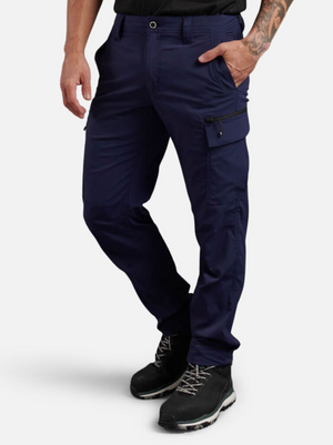 A person in dark blue King Gee Trademark Cargo Pants stands with a tattooed arm and black work boots. Their left hand is in the pocket. The pants, made from durable Ripstop fabric, have a side pocket with a zipper.