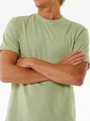 A person stands with arms crossed, slightly turned to the side, wearing a light green Rip Curl Plain Wash Tee with a relaxed fit against a plain, light background.