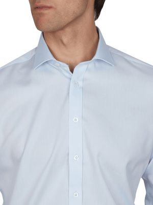 A man wears the Abelard Non Iron Cotton Twill Slim Fit Shirt in light blue with a cutaway collar, buttoned up, shown from shoulders to above the mouth against a plain white background.