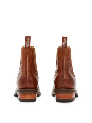 A rear view of brown leather RM Williams Lady Yearling Rubber Sole Boot ankle boots with stacked heels and pull tabs featuring white cursive writing, set against a plain white background.