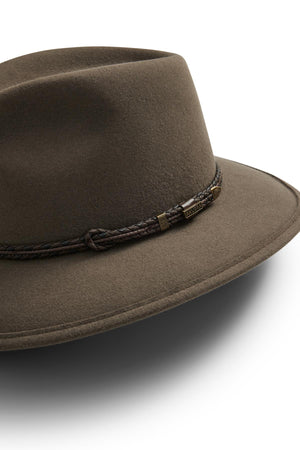 A close-up of the Akubra Traveller hat, featuring brown felt, a braided leather band, and a small metallic tag, showcases its distinct structure against a white background.