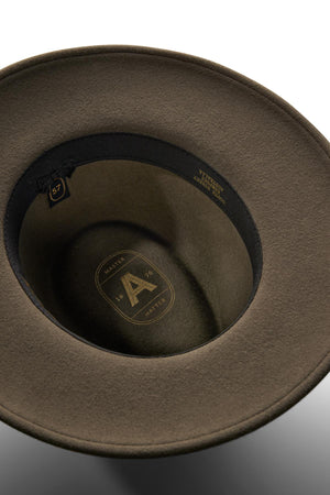 A close-up of the Akubra Traveller reveals its brown felt construction, black inner band, size label “57,” and gold branding with the model name on the inside crown.