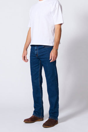 Wearing a plain white t-shirt, brown boots, and AMCO Stretch Regular Fit Jean in indigo wash, a person stands against a light background with their face not visible.