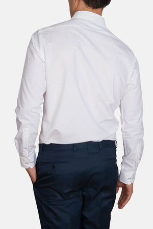 A person wearing a slim fit, white Abelard 4 Way Stretch Poplin Slim Fit dress shirt and dark blue trousers is shown from the back. The wrinkle-resistant shirt has long sleeves with cuffs, and the trousers have buttoned back pockets. The person stands with one hand in their pocket.