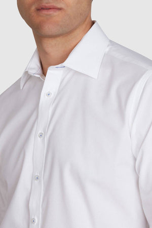 A person wearing a neatly pressed Abelard 4 Way Stretch Poplin Slim Fit white dress shirt with a spread collar. The buttoned-up shirt emphasizes its wrinkle-resistant quality. The image captures the upper torso and part of the person's face, though the face is partially out of frame, against a plain light gray background.
