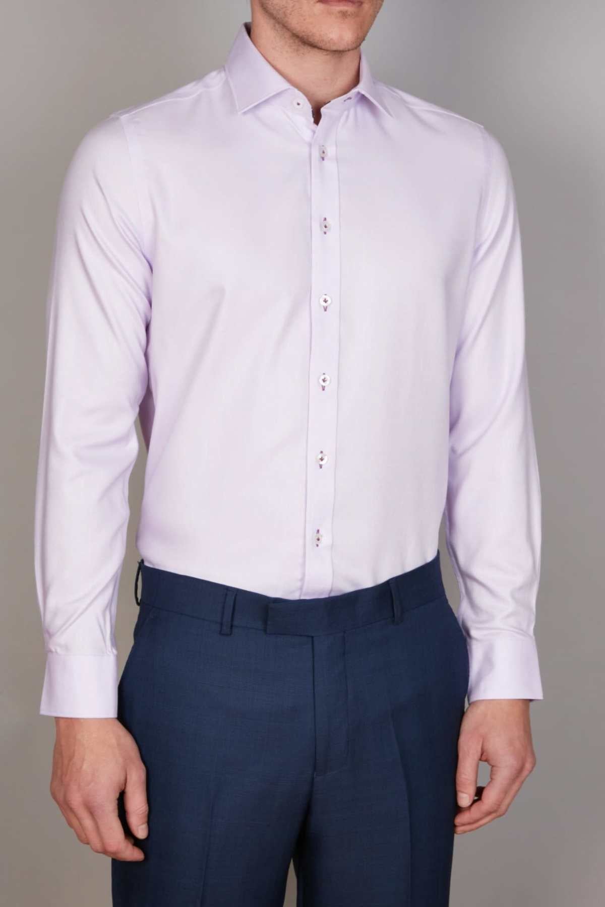 A person standing against a neutral background is wearing an Abelard Non Iron Cotton Twill Slim Fit Shirt in light lavender with a cutaway collar and dark blue trousers. The shirt features buttoned cuffs, and the face of the person is not visible in the image.