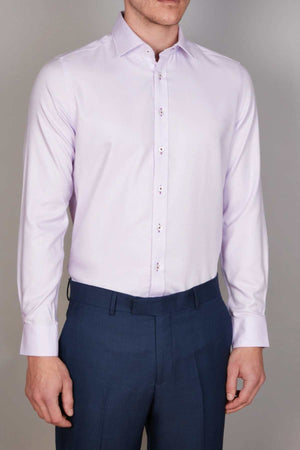 A person standing against a neutral background is wearing an Abelard Non Iron Cotton Twill Slim Fit Shirt in light lavender with a cutaway collar and dark blue trousers. The shirt features buttoned cuffs, and the face of the person is not visible in the image.
