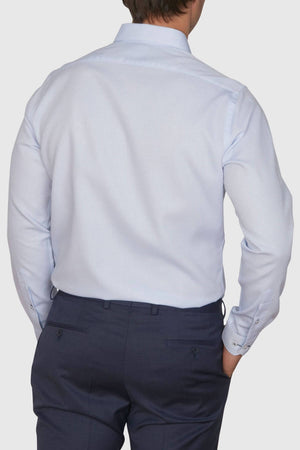 A person is shown from the back wearing the Abelard Waffle Dobby Slim Fit Shirt in light blue with dark trousers. Their right hand rests in their pocket, allowing the 100% cotton shirt to drape comfortably as they stand against a plain, light gray background.