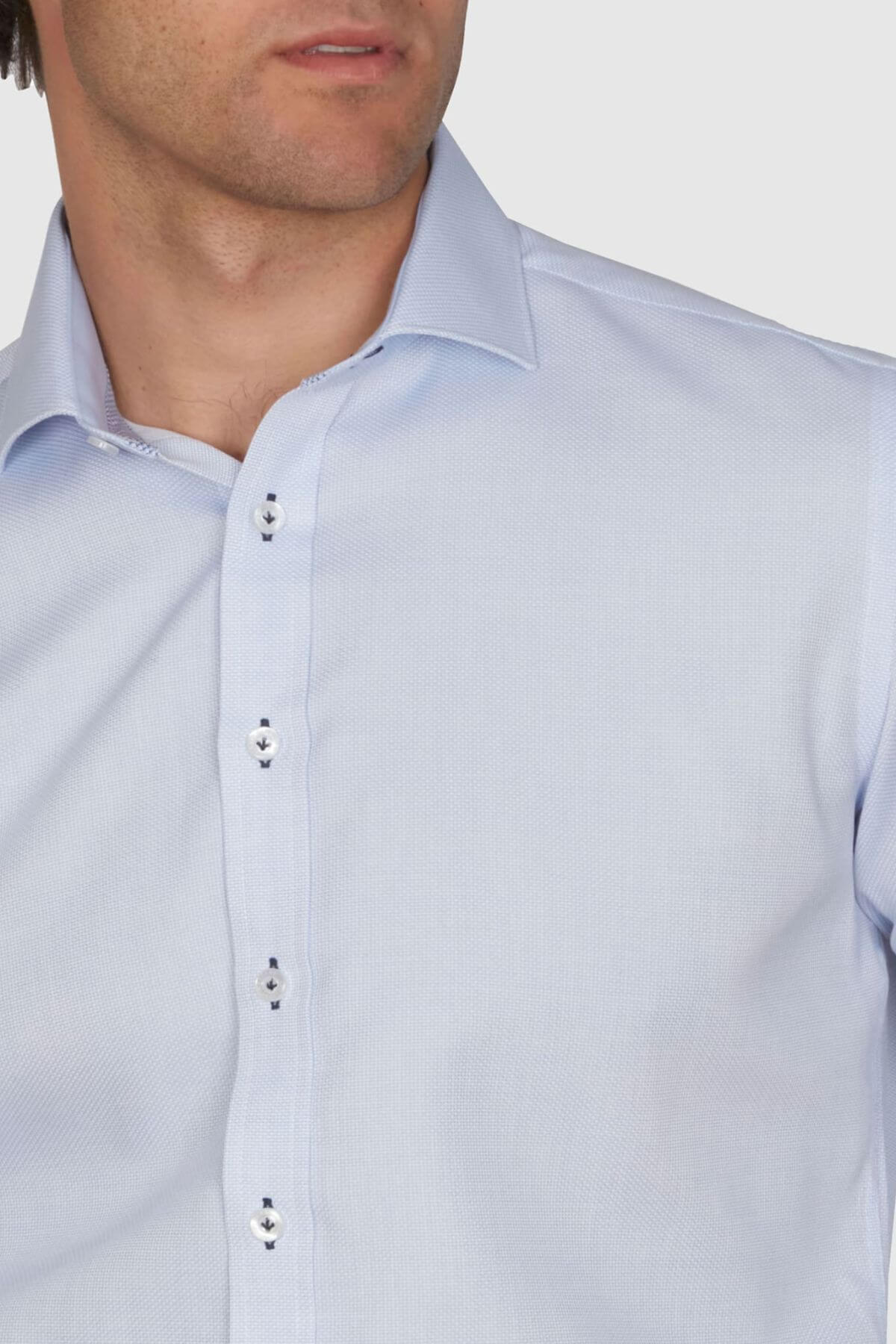 A person wears the Abelard Waffle Dobby Slim Fit Shirt, light blue with a spread collar and black-silver buttons. Made of 100% cotton with a waffle dobby design, it is buttoned up from shoulders to chest against a plain background.