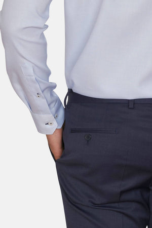 A person in a light blue Abelard Waffle Dobby Slim Fit Shirt with buttoned cuffs and dark trousers with a rear pocket has their hand in the pocket. The shot focuses on the back, highlighting the 100% cotton fabric's waffle dobby design and detailed craftsmanship.