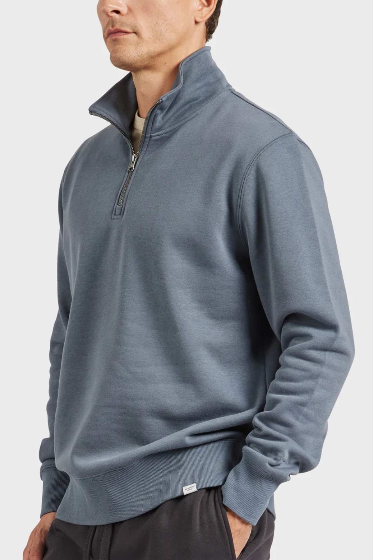 A person is wearing the Academy Brand 1/2 Zip Sweat in light blue brushed fleece, with their hands in the pockets of black pants. The plain white background emphasizes the attire.