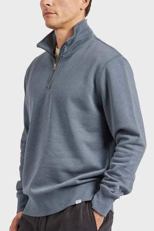 A person is wearing the Academy Brand 1/2 Zip Sweat in light blue brushed fleece, with their hands in the pockets of black pants. The plain white background emphasizes the attire.