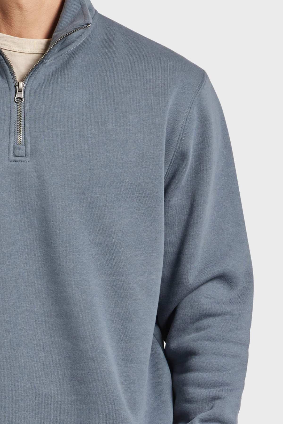 A person is wearing the Academy Brand 1/2 Zip Sweat in light blue with a white undershirt visible at the neckline. The image focuses on the upper torso and part of the neck, emphasizing the sweatshirt's premium brushed fleece material and detailed zipper.