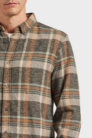 A person wearing an Academy Brand Aspen Shirt featuring a brown, green, and white yarn dye twill check. The button-up with a point collar is shown against a plain white background, capturing the upper torso and part of the person's face.