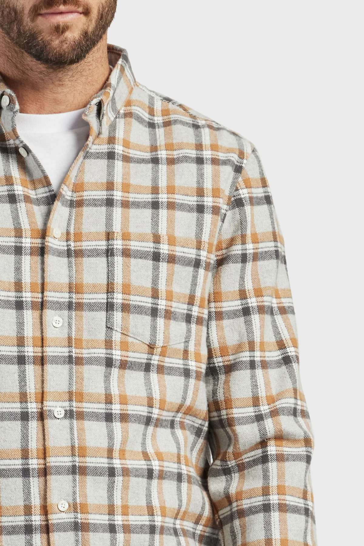 A man wears the Academy Brand Boston Shirt—100% cotton yarn-dye check flannel in beige, gray, and white—over a white T-shirt. Only the lower half of his face and upper torso are visible.