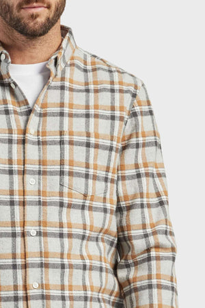 A man wears the Academy Brand Boston Shirt—100% cotton yarn-dye check flannel in beige, gray, and white—over a white T-shirt. Only the lower half of his face and upper torso are visible.
