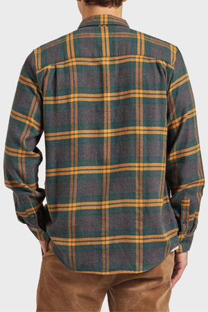A person is seen from behind in an Academy Brand Denver Shirt featuring green, yellow, and brown plaid. This cotton shirt has long sleeves and is paired with tan pants against a plain light-colored background.