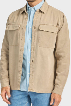 A man shown from shoulders to hips wears the Academy Brand Essential Overshirt with double chest flap pockets, layered over a light blue collared shirt and blue jeans.
