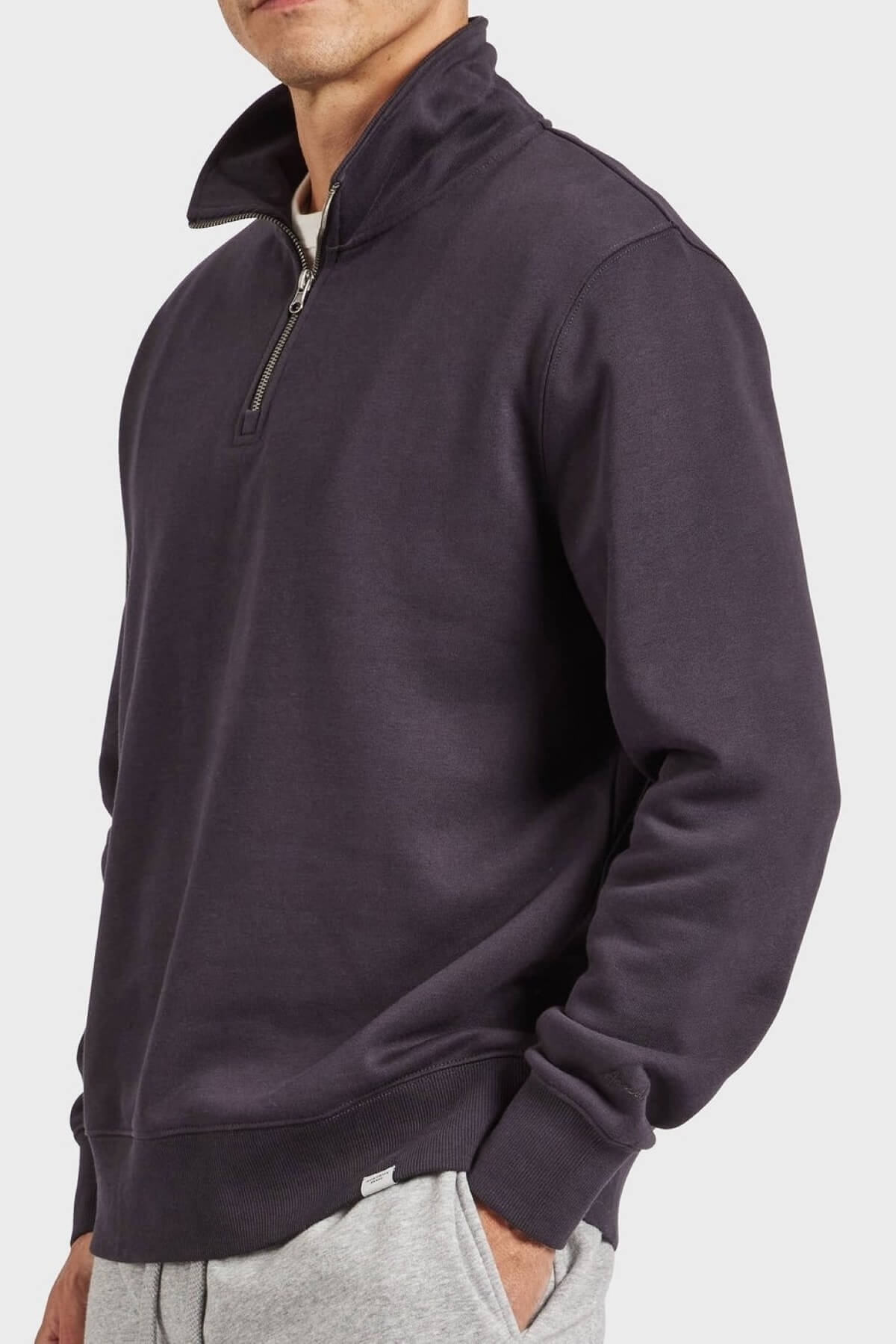 A man wearing an Academy Brand 1/2 Zip Sweat in dark navy and light gray sweatpants, with his left hand in his pocket, stands against a plain light background.