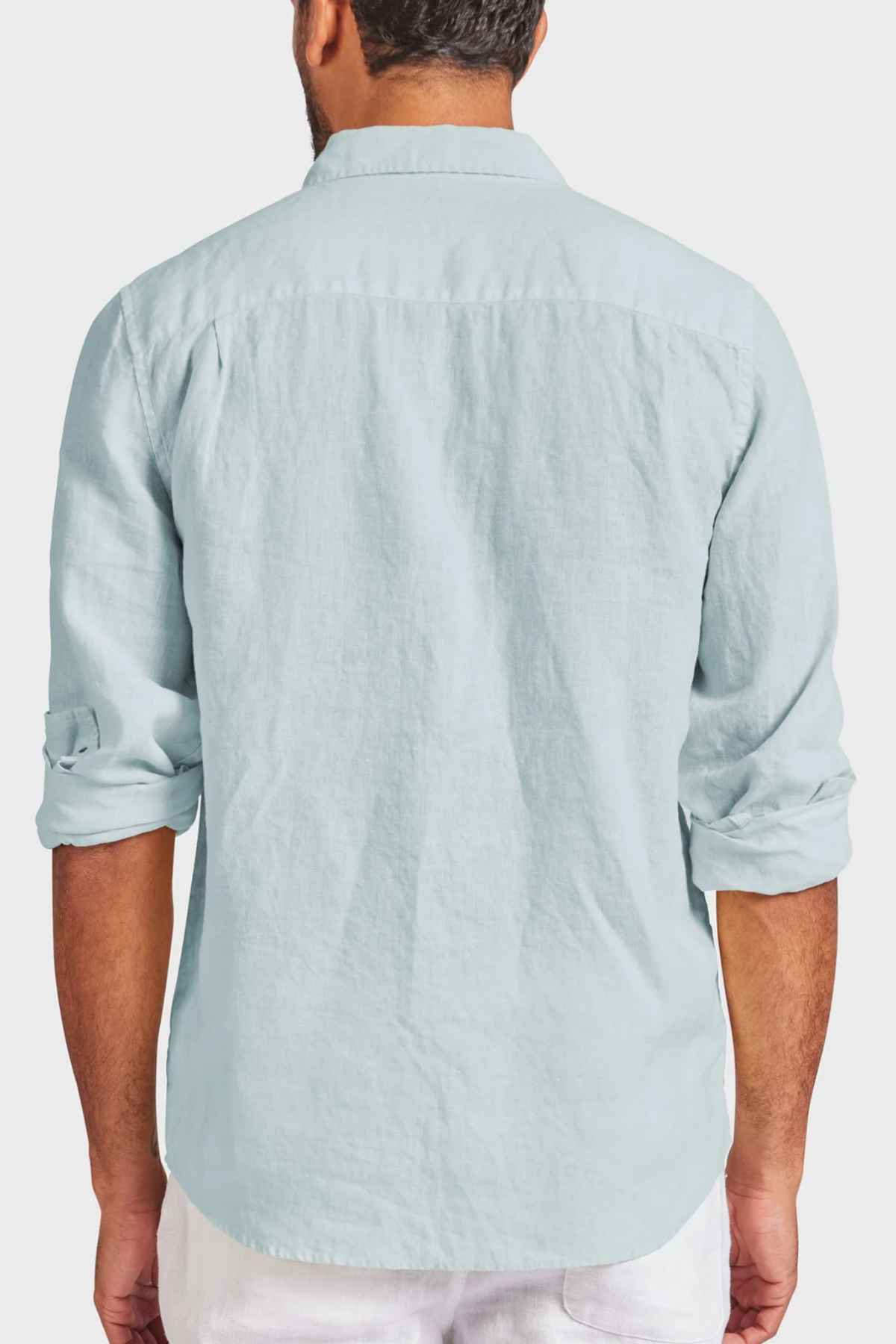 A person with short, dark hair is wearing an Academy Brand Hampton Linen Shirt in light blue, featuring a classic point collar and rolled-up sleeves, paired with white pants. The view is from the back against a plain white background.