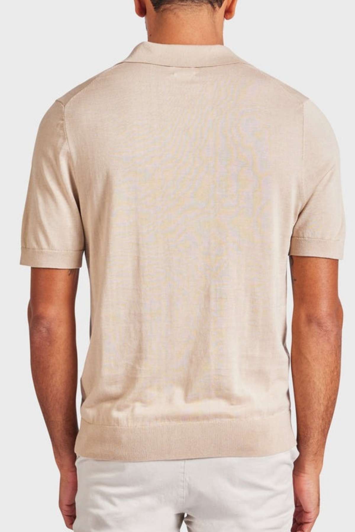 A person wearing a light beige short-sleeve Academy Brand Irvine Knit Polo and white pants is depicted from the back, standing against a plain background.