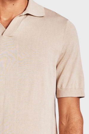 Close-up of a person wearing the Academy Brand Irvine Knit Polo in light beige with short sleeves. The person's left arm is visible, showing part of their upper torso. The background is a plain, light color.