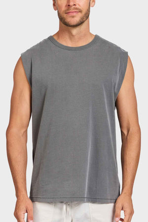 A man stands against a white background, dressed in the Academy Brand Jimmy Muscle Tee in gray along with light-colored shorts. With short hair and a light beard, his arms rest relaxed at his sides while he gazes forward. The tee, crafted from 100% cotton, offers both comfort and style.