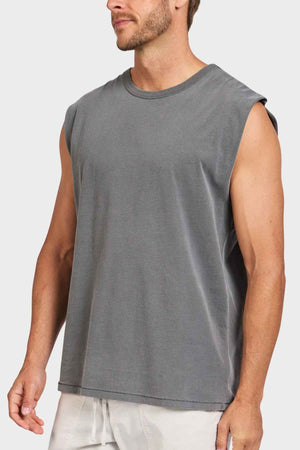 An individual in a sleeveless Academy Brand Jimmy Muscle Tee of gray hue stands against a minimalist background. The T-shirt, made from 100% cotton, is designed to be loose-fitting and casual. The person has short hair and stubble, with their hands resting at their sides.