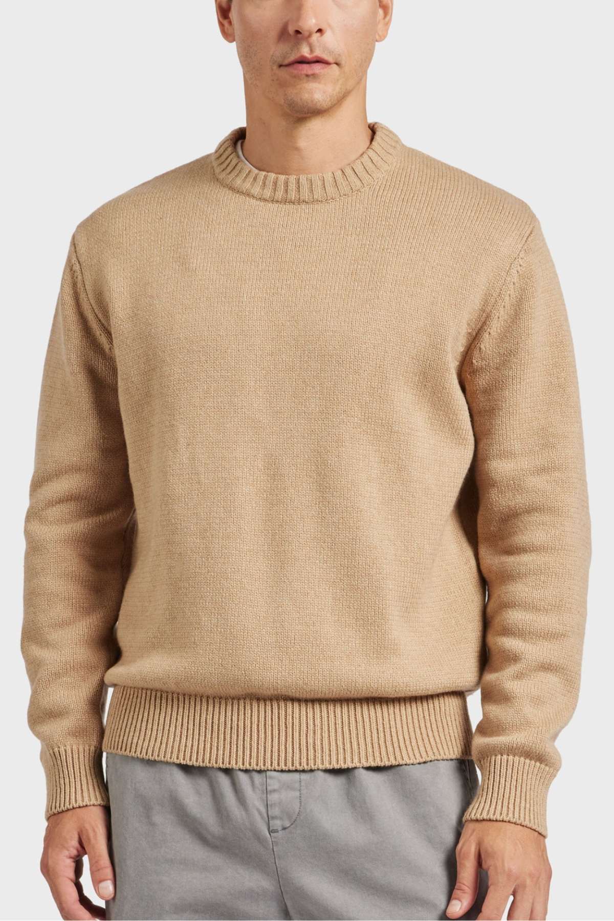 A person is wearing the high-quality, slightly oversized Academy Brand Malibu Crew beige knit sweater with ribbed cuffs, neckline, and hem. They are also sporting gray pants, standing against a plain white background. This cozy look offers ultimate comfort and style.
