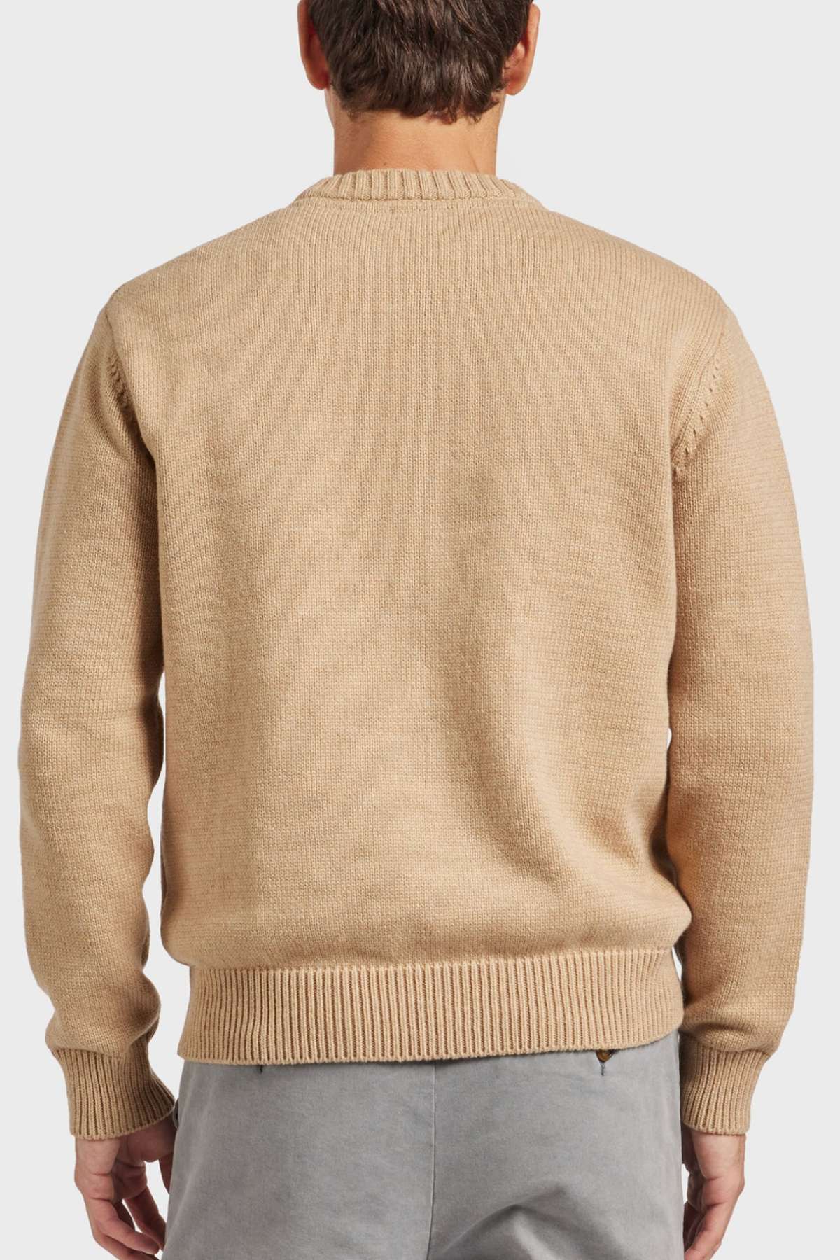 A person is sporting the Academy Brand Malibu Crew sweater, which comes in a light brown knit fabric and features a ribbed hem and cuffs. The sweater has a slightly oversized fit, showcased from the back in the image. The individual is also donning light gray pants against a plain white backdrop.
