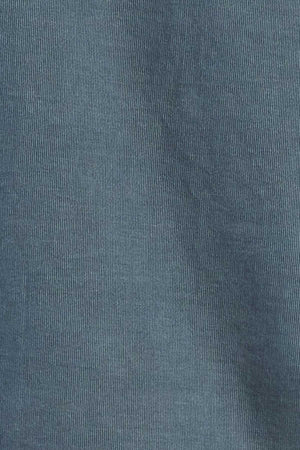 A close-up view of the teal-colored, 100% cotton corduroy fabric from the Academy Brand Micro Cord Shirt, highlighting its characteristic vertical ridged pattern and texture. The fabric appears soft and slightly worn, complemented by imitation mother-of-pearl buttons.