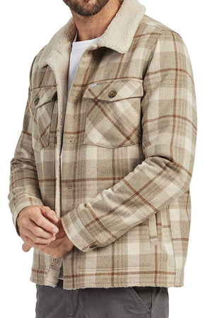 Man wearing the Academy Brand Quincy Jacket in beige and brown plaid, crafted from a wool blend with a white faux shearling collar, styled with a white undershirt and gray pants. The jacket has buttoned chest pockets; man's face is partially out of frame.