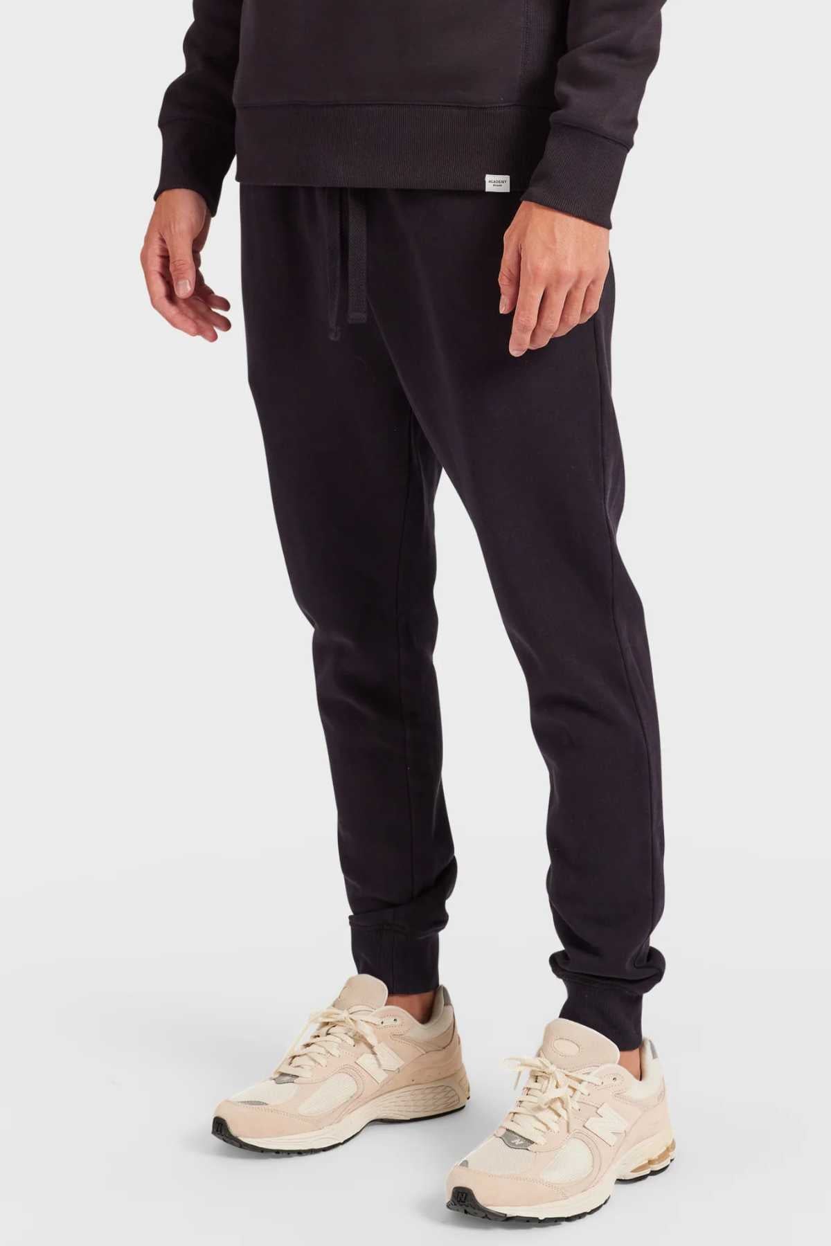 A person in Academy Brand Sweat Pant with a premium brushed fleece texture and an elastic waist is wearing beige sneakers. The focus is on the lower half against a plain white background.