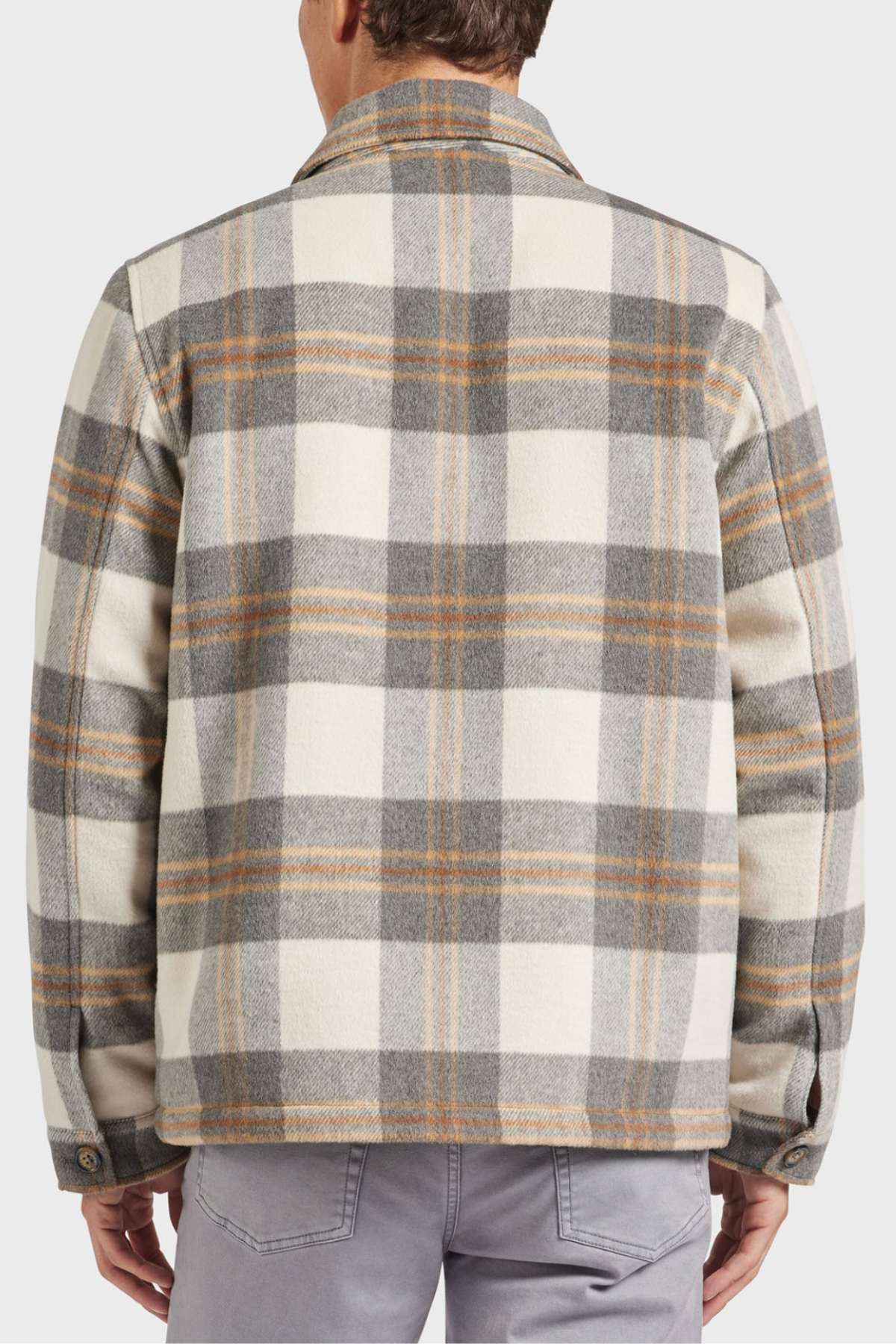 A person wearing an Academy Brand Tulsa Jacket in plaid wool blend with gray, white, and brown tones stands facing away. The jacket features a classic collar, buttoned cuffs, and quilted lining, paired elegantly with light gray pants.